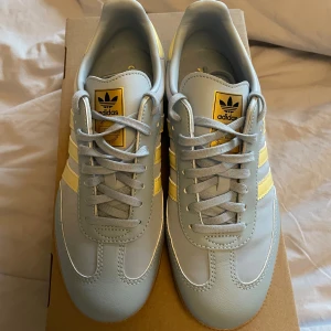Adidas Samba ljusblå och gula sneakers - Säljer ett par Adidas Samba sneakers i ljusblått med ljusgula detaljer och klassiska tre ränder. Skorna är köpta för bara någon månad sen och är använda två gånger. De har ljusblå snörning och beige sula! Skorna har inga deffekter!