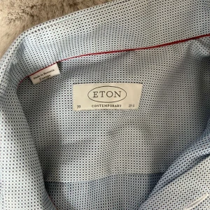 Ljusblå mönstrad skjorta från Eton - Snygg ljusblå skjorta från Eton i contemporary fit med diskret småmönstrat tryck och klassisk krage. Skjortan har vita knappar och en röd detaljsöm på insidan av kragen. Perfekt för dig som gillar stilrena och moderna plagg.