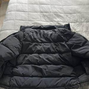 Svart pufferjacka från Trapstar - Säljer en svart pufferjacka från Trapstar med broderad logga på bröstet och stor Trapstar-text på insidan. Jackan har dragkedja framtill, hög krage och två fickor. Perfekt för kalla dagar och riktigt street i stilen. Lite smutsig därav priset. Går lätt att bara tvätta bort med vatten, jag har inte orken då jag bara vill få bort massor kläder