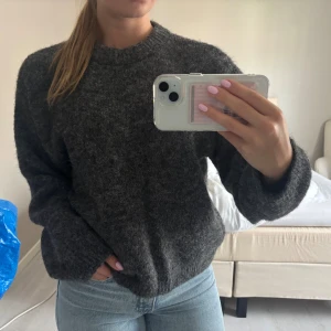 Mörkgrå stickad tröja med rund hals - Mysig mörkgrå stickad tröja med rund halsringning och långa ärmar. Tröjan har en lite loose passform och är perfekt för kyliga dagar. Den är enkel att matcha med jeans eller kjol och har en klassisk, tidlös look. (Använd en gång)