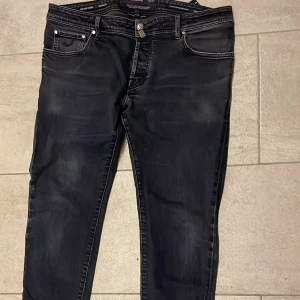 Svarta jeans från Jacob Cohën, stl 38 - Snygga svarta jeans från Jacob Cohën med klassisk femficksdesign och coola detaljer som märkets logoknapp och exklusiva sömmar. Jeansen har en smal passform och är tillverkade i bomull med en touch av stretch för extra komfort.