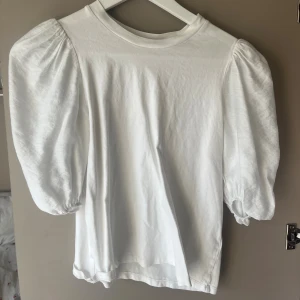 Vit puffärmad topp från Kappahl XS - Säljer en vit topp från Kappahl i storlek XS. Toppen har puffiga trekvartsärmar med resår vid ärmslut och en klassisk rund halsringning. Tillverkad i mjuk bomull, perfekt för en clean och trendig look.