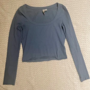 Blå ribbad långärmad topp - Säljer en ljusblå ribbad topp från H&M med lång ärm och rundad urringning. Toppen är croppad och har en slim passform som sitter snyggt på kroppen. Perfekt att styla med jeans eller kjol för en trendig look.