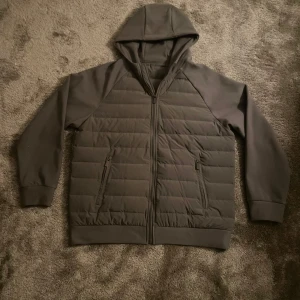 Mörkgrå hoodie med quiltad front L - Snygg mörkgrå hoodie med quiltad front och dragkedja hela vägen. Tröjan har huva, långa ärmar och två praktiska fickor med dragkedja. Perfekt för kyliga dagar när du vill ha en stilren och bekväm look. Ny slick använd 2 gånger.