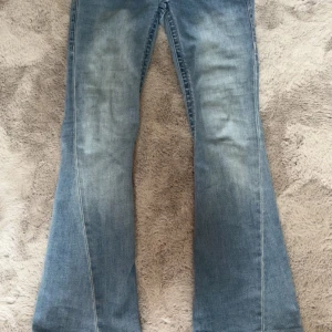 True Religion Joey ljusblå flare jeans - Säljer ett par ikoniska True Religion Joey jeans i ljusblå tvätt med snygg flare och låg midja. Jeansen har klassiska detaljer som markerade bakfickor med lock och silverknappar samt patch med logga bak. Perfekta för dig som gillar retrovibbar och statement-jeans.