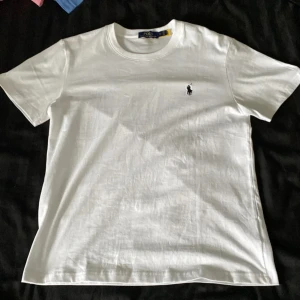 Vit t-shirt från Polo Ralph Lauren - Mer som S. Vit t-shirt från Polo Ralph Lauren med klassisk rund hals och korta ärmar. På bröstet finns den ikoniska broderade polospelaren i svart. T-shirten är gjord i mjuk bomull och har en clean, stilren look som funkar till allt.