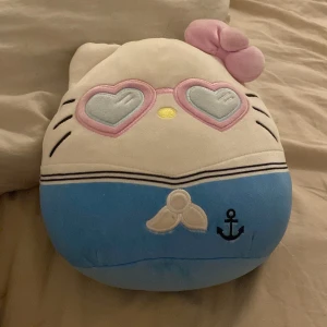 Hello Kitty Sailor Squishmallow - Söt Hello Kitty Squishmallow i sjömansdräkt med hjärtformade glasögon. Mjuk och kramvänlig, perfekt för samlare eller som mysig kudde. Viss missfärgning på baksidan (se bild), annars i gott skick. Originalmärkning kvar på etiketten.