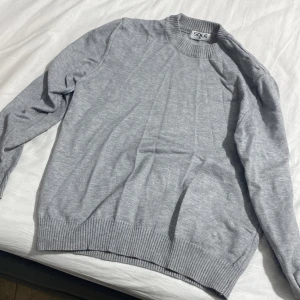 Grå stickad tröja från SOLE - Snygg grå stickad tröja från SOLE i storlek M. Tröjan har rund hals med ribbad kant och långa ärmar. Perfekt för dig som gillar enkel och clean stil. Materialet känns mjukt och skönt mot huden och passar bra till jeans eller chinos.