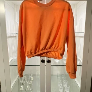 Orange sweatshirt från Pull&Bear - Säljer en orange sweatshirt från Pull&Bear i storlek M. Tröjan har lång ärm, rund hals och resår i midjan för en snygg passform. Perfekt för dig som gillar en enkel men färgstark stil.