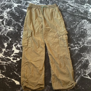 Beiga cargopants med dragsko - Säljer ett par beiga cargopants med elastisk midja och dragsko. Byxorna har stora fickor på sidorna och justerbara benslut. Tillverkade i bomull, perfekta för en avslappnad och chill stil.