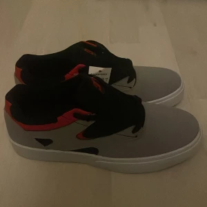 DC Shoes sneakers grå och svart - Snygga sneakers från DC Shoes i grått och svart med röda detaljer. Skorna har en låg profil, vit platt sula och klassisk snörning. Ovandelen är i syntetmaterial och textil, med DC-logga broderad på plösen. Perfekta för dig som gillar streetstyle. Dem är helt o använda, box medföljer ej. Priset går att diskutera 