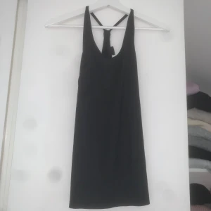 Svart sportlinne  - Svart, sportlinne från TTL med smala axelband som korsas i ryggen och knytdetalj. Linnet är ärmlös och har en stilren passform i stretchigt material som passar perfekt för träning eller en aktiv dag.