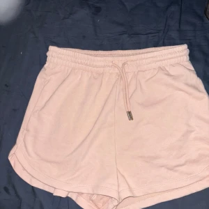 Ljusrosa mjuka shorts med snörning - Säljer ett par ljusrosa shorts i mjuk bomull med elastisk midja och snörning framtill. De har en avslappnad passform och är perfekta för varma dagar eller chill hemma. Priset går att diskutera!