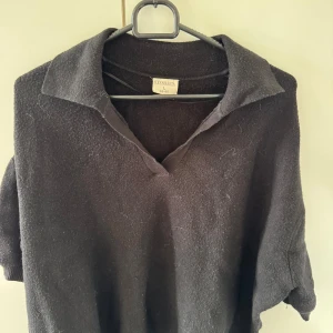 Svart stickad polotröja från Stories - Svart stickad polotröja från Stories i storlek L. Tröjan har en klassisk krage med v-ringning och kortare ärmar. Perfekt för dig som gillar en stilren och enkel look med en twist. Materialet är mjukt och passar bra till lager-på-lager.