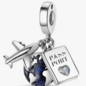 Pandora berlock med flygplan och pass - Superfin Pandora-berlock i silverfärg med detaljer som ett flygplan, ett pass och en blå jordglob. Perfekt för dig som älskar att resa och vill ha ett unikt smycke på armbandet. Kommer i söt rosa presentask med rosett.