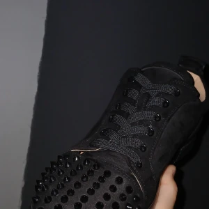 Christian Louboutin svarta sneakers med nitar - Säljer ett par svarta sneakers från Christian Louboutin i mocka med svarta nitar på tån. Skorna har snörning och den klassiska röda sulan med logotyp. Kommer med originalkartong och dustbag. Perfekt för dig som vill sticka ut med lyxiga detaljer.