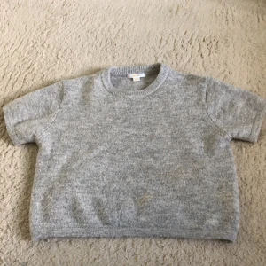 Grå stickad croppad tröja Gina Tricot - Grå stickad tröja från Gina Tricot med kort ärm och croppad passform. Mjuk och mysig, perfekt till jeans eller kjol. Rund halsringning och enkel design som är lätt att matcha.