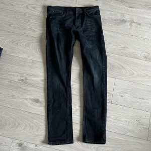 Svarta jeans från Nudie Jeans Co W32 L34 - Snygga mörka jeans från Nudie Jeans Co i klassisk rak modell. Jeansen har fem fickor, normal passform och är tillverkade i slitstarkt bomullstyg. Perfekta för dig som gillar stilrena och tidlösa jeans med en mörk tvätt.