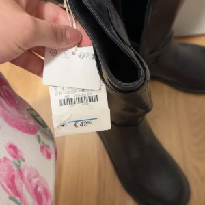 Svarta boots från Zara med gulddetaljer - Snygga svarta boots från Zara i skinnimitation med rund tå och platt sula. Dekorativa remmar med små guldfärgade spännen ger en stilren look. Perfekta till höstens outfits och funkar till många olika stilar.