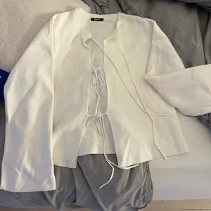 Vit kofta med snörning från Gina Tricot - Vit kofta från Gina Tricot med snygg snörning framtill. Tröjan har långärmade ärmar och är gjord i mjukt stickat material. Perfekt för dig som gillar en clean och stilren look med en twist. Passar till jeans eller kjol för en chill vibe.