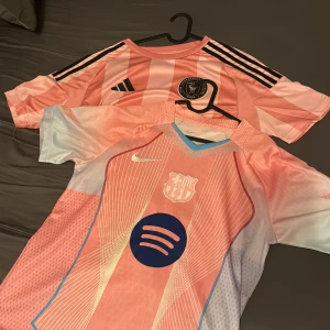Barça och Inter Miami rosa fotbollströjor S - Två snygga fotbollströjor i rosa toner: FC Barcelona Nike-tröja med Raphinha 11 och Spotify-logga, samt Inter Miami Adidas-tröja med svarta ränder och klubbmärke. Båda i funktionsmaterial, kortärmade och med sportig passform. Perfekt för dig som älskar fotboll och vill sticka ut.