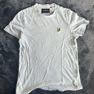 Vit t-shirt från Lyle & Scott, M - Vit t-shirt från Lyle & Scott i mjuk bomull. Klassisk rund hals och korta ärmar. På bröstet sitter den ikoniska broderade fågeln i gult och svart. Enkel och stilren design som funkar till allt. Perfekt för dig som gillar cleana plagg med diskret logga.