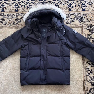Canada Goose Wyndham Parka - Säljer min Canada Goose Wyndham Parka i svart, storlek S. Den har bara använts en vinter och har alltid förvarats på ett bra sätt, så den är i mycket bra skick. Jackan har avtagbar päls på huvan, hög krage, varm dunfyllning och det klassiska Canada Goose-märket på ärmen. Dragkedja och knappar fungerar perfekt. En riktigt snygg och varm vinterjacka som kombinerar stil och kvalitet.