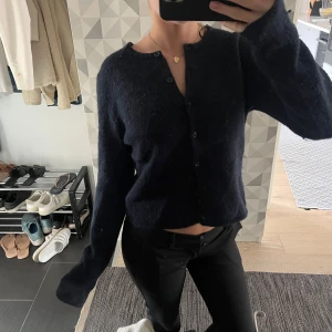 Mörkblå kofta med knappar - Snygg mörkblå kofta med rund hals och knappar framtill. Tröjan är lite croppad och har långa ärmar. Materialet känns mjukt och lite fluffigt, perfekt för kyliga dagar. Enkel och stilren design som passar till svarta jeans eller kjol.