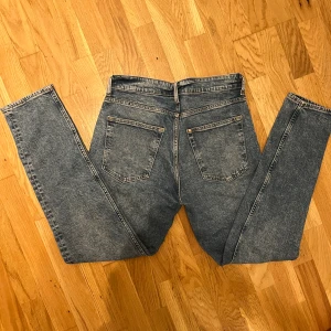 Blå tapered jeans med klassisk tvätt - Snygga blå jeans med tapered passform och klassisk femficksdesign. Jeansen har normalhög midja, dragkedja och knapp framtill samt subtila slitningar för en cool look. Perfekta till sneakers och hoodie för en avslappnad stil. Aldrig använda från HM