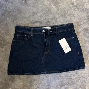 Mörkblå jeanskjol från Zara - Snygg mörkblå jeanskjol från Zara med klassisk femficksdesign, gylf med knapp och bälteshällor. Kjolen har raka linjer och kontrastsömmar som ger en cool denimlook. 