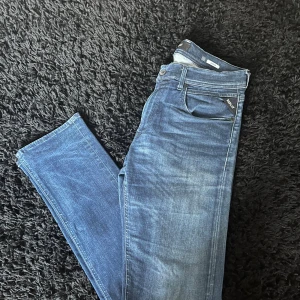 Replay Grover jeans blå 32 - Snygga Replay Grover jeans i klassisk blå tvätt med lätt slitning. Modellen har raka ben, normal passform och fem fickor. Jeansen är tillverkade i mjukt denim-material med knapp och dragkedja i midjan. Perfekt för dig som gillar stilrena och bekväma jeans. Kan gå ner i pris vid snabb affär!! 