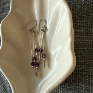 Långa örhängen med lila pärlor - 🫧 Säljer ett par snygga långa örhängen i silverfärgad metall med tre tunna hängande kedjor på varje örhänge.  🫧 Varje kedja har små lila pärlor och silverfärgade detaljer.  🫧 Perfekt för dig som gillar statement-smycken med lite färg.  🫧 Köpte utomlands. Mycket bra kvalité. Fint skick