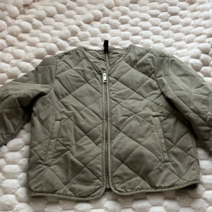 Quiltad jacka i XXS - Snygg quiltad jacka i  med raka linjer och dragkedja framtill. Jackan har två fickor och lång ärm, perfekt för lager-på-lager. Den har ett stilrent rutmönster och är tillverkad i mjukt bomullsmaterial. Enkel och clean look som passar till det mesta.