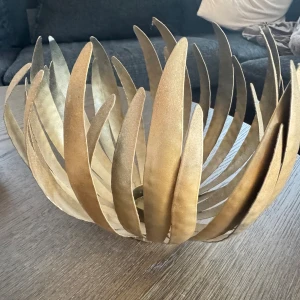 Ljushållare i guldmetall  - Bilderna visar en dekorativ ljushållare i guldmetall med bladformad design. Produkten har en modern och elegant look, perfekt som bordsdekoration. Inga synliga defekter eller slitage. Passar utmärkt för hemmet som stilfull inredningsdetalj.