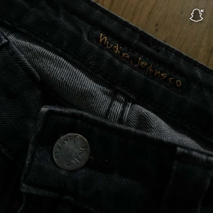 Svarta jeans från Nudie Jeans - Snygga svarta jeans från Nudie Jeans med klassisk femficksdesign och subtila slitningar. Jeansen har en rak passform och är tillverkade i mjukt denimtyg med svarta sömmar och detaljer. Perfekt för dig som gillar stilrena och tidlösa jeans. STORLEK W29 L29