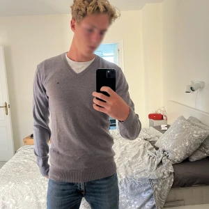 Grå v-ringad tröja från J.Lindeberg - Snygg grå v-ringad tröja från J.Lindeberg i 100% merinoull. Diskret broderad logga på bröstet och ribbade muddar vid ärmslut och nederkant. Perfekt för dig som gillar stilrena och klassiska plagg med en modern touch.