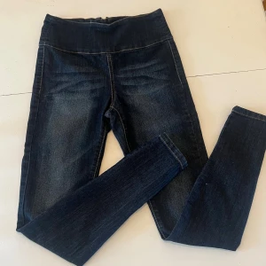 Mörkblå skinny jeans - Mörkblå jeans med hög midja och dragkedja bak. Tight passform med klassiska bakfickor och lätt slitna detaljer framtill. Perfekta för dig som gillar en smal siluett och stretchigt material. Vet inte vilken storlek det är men ca stl 36.