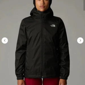 Svart vindjacka från The North Face - Svart vindjacka med huva från The North Face. Jackan har dragkedja framtill, elastiska muddar och logga på bröstet och ryggen. Snygg och enkel design som funkar till allt. Tillverkad i lätt polyester och har normal passform.