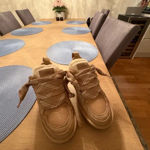 Beige UGG lowmel - Säljer ett par snygga beige sneakers från UGG med breda snören och grov sula. Ovandelen är i mocka och textil, och insidan är fodrad med mjuk ull för extra komfort. Perfekta för dig som vill ha både stil och värme under höst och vinter. Kolla diefekter på sista bilden ( missfärgning ifrån jeans men inget man lägger märke till )🥰