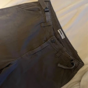 Mörkgråa cargopants  - Säljer ett par mörk gråa cargopants  med klassiska fickor på sidorna och baktill. Byxorna har snörning i midjan och bälteshällor för extra stil. Materialet är mjukt och känns skönt mot huden, perfekt för en chill look.