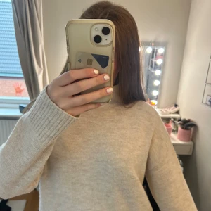 Beige stickad tröja från Kappahl - Mysig beige stickad tröja från Kappahl i storlek XS. Tröjan har en högre hals, ribbade muddar och avslut, samt en loose fit som ger en chill vibe. Perfekt att slänga på sig när det är kallt ute.