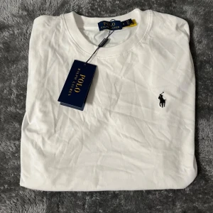  Polo Ralph Lauren T-shirt  - Klassisk vit t-shirt från Polo Ralph Lauren med rund hals och kort ärm. Ikoniska broderade loggan på bröstet. Tillverkad i mjuk bomull för en skön känsla. Perfekt basic-plagg med stilren design. Pris kan diskuteras. 