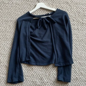 Mörkblå kofta med rosett/knyt - ALDRIG ANVÄND. Säljer en mörkblå kofta från 157 i mjukt material. Toppen har långa ärmar och en snygg knytning framtill vid halsen. Perfekt att styla över ett linne eller t-shirt för en chill look. Croppad passform som ger en trendig vibe.