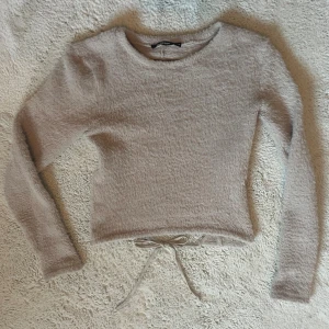 Beige rygglös tröja - Supermjuk och fluffig beige tröja från Bikbok med lång ärm och rund hals. Tröjan har ett snyggt knytband i midjan och en öppen rygg som ger en cool touch. Perfekt för dig som gillar mysiga och trendiga plagg med lite extra detaljer. Storlek M, me passar bra på S och även Xs