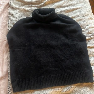 Svart polotröja i stickat material - En svart polotröja i stickat material med hög, ribbad krage. Tröjan har en klassisk och enkel design utan synliga detaljer eller mönster, perfekt för lager-på-lager under kyliga dagar.