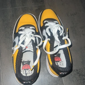 Nike Air Force 1 gul/svart sneakers - Nike Air Force 1 sneakers med en fet färgkombo i gult, svart och vitt. Skorna har klassisk snörning, rund tå och platt sula. Ovandelen är i skinn och mesh med basketbollgrafik på innersulan. Swoosh-loggan syns tydligt på sidan. Perfekt för dig som vill sticka ut.