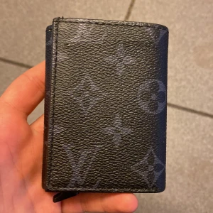 Louis Vuitton svart plånbok i skinn - Säljer en svart plånbok från Louis Vuitton med klassiskt monogrammönster. Plånboken är tillverkad i skinn och har plats för flera kort. Perfekt storlek för fickan och stilren design med diskreta LV-detaljer.