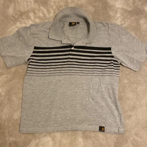 Grå Carhartt T-shirt med krage - 100% bomull, är S men sitter kanske liter som en XS. Är öppen för ett lägre pris vid snabb affär. Om ni har några frågor skriv gärna!