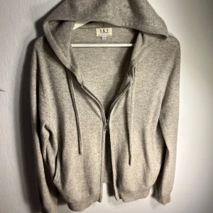 Ljusgrå Kashmir ziphoodie - Ljusgrå hoodie från S&T Clothing i en lyxig blandning av merinoull och kashmir. Tröjan har två dragkedjor framtill, huva med snörning. Nypris på över 2000kr. Väldigt bra skick men ändå lite tecken på användning som knappt märks