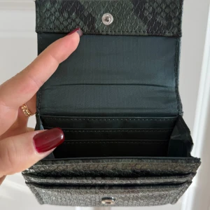Grön plånbok med ormmönster - Snygg grön plånbok från dondonna med ormmönstrad yta och praktisk knappstängning. Köpt för ungefär 800 ! 